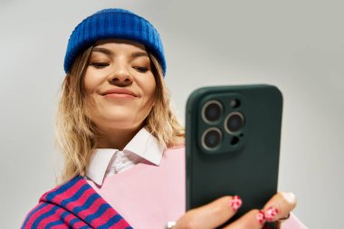 Şık giyinmiş genç bir kadın akıllı telefonuna poz verirken özgüvenle bakıyor..