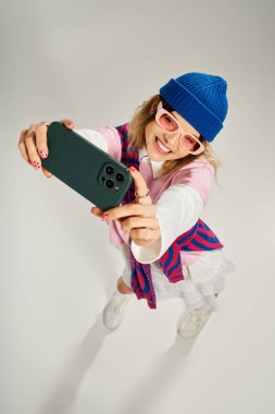 Mavi bereli güzel genç bir kadın parlak bir stüdyoda eğlenceli bir selfie çekiyor..