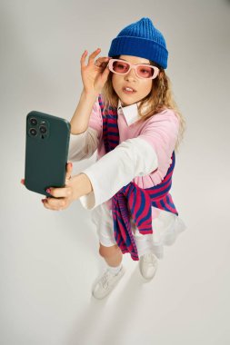 Modern bir stüdyoda, şık bir genç kadın moda gözlük takarken selfie çekiyor..