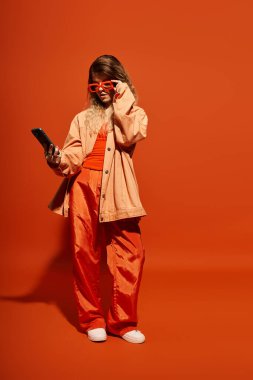 Portakal rengi şık bir elbise giymiş güzel bir kadın telefonunu kontrol ediyor, ışık saçıyor..