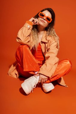 Parlak giyimli genç bir kadın turuncu renkli bir arka planda kendine güvenin tadını çıkarıyor..