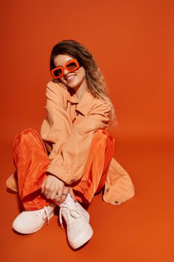 Tarz sahibi genç bir kadın turuncu bir arka planda neşeli bir hava yakalar..