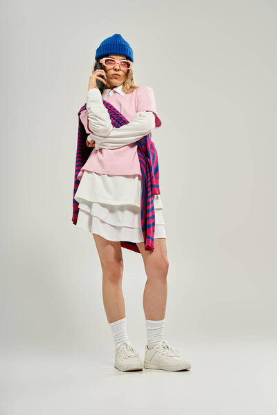 A young woman wearing a blue beanie and stylish attire stands confidently in a studio.