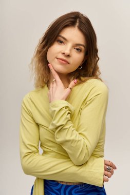 Çekici genç kadın, eşsiz moda anlayışını sergiliyor. Gri bir arkaplanda zarif bir duruşu var..