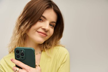 Şık giyinmiş neşeli genç bir kadın akıllı telefonunu kendine güvenle tutuyor, büyüleyici bir şekilde..