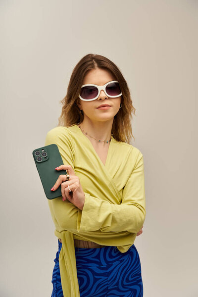 Красивая молодая женщина уверенно позирует в ярком наряде на гладком сером фоне.