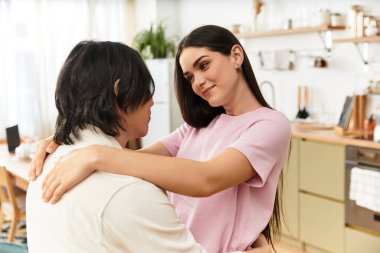 Çiftler birbirlerine davetkar yaşam alanlarında sarılırlar, birbirlerine sevgi dolu bakışlar ve gülümsemeler atarlar..