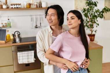 Bir erkek ve bir kadın, davetkar mutfaklarında gülümserken şefkatli bir kucaklaşmayı paylaşırlar..