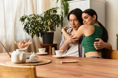 Sıcak, ahşap bir masada oturan bir çift kahve yudumlarken şefkatli bir kucaklaşmanın tadını çıkarıyor..