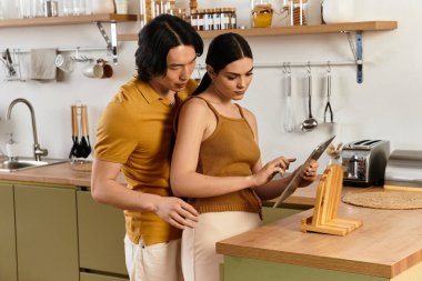 Bir çift, sıcak mutfaklarında bir tablet üzerinde yemek tariflerini incelerken hassas bir anı paylaşıyor..