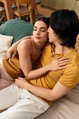 Bir çift kanepede şefkatle kucaklaşıyor, derin sevgilerini ve ilişkilerini sessiz bir evde sergiliyorlar..