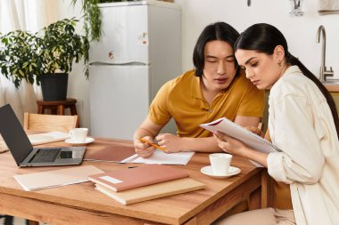 Bir çift ahşap bir masada oturuyor, notlar ve dizüstü bilgisayarla işbirliği yapıyorlar..