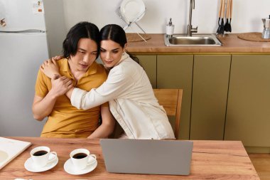 Sevgi dolu bir çift, ahşap bir masada oturur, bir dizüstü bilgisayarla uğraşırken gülümseme ve kahveyi paylaşır..