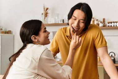 Sevgi dolu bir çift, evde keyifli bir anın tadını çıkarır. Birbirlerine ikram ederler ve sıcak bir gülümseme sergilerler..