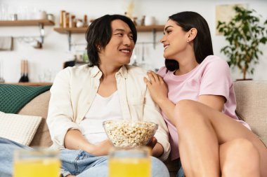 Bir erkek ve bir kadın patlamış mısır ve kahkahaların tadını çıkarırken kanepede hassas bir anı paylaşıyor..