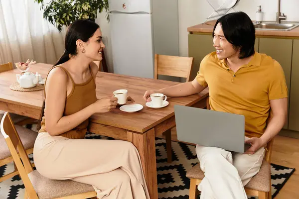 Mutfak masasında sıcak bir ortamda kahvelerini yudumlarken bir kadın ve bir erkek sıcak bir gülümseme paylaşır..