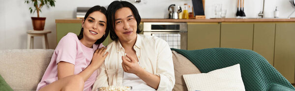 Loving couple relaxes together on a cozy sofa, sharing smiles and snacks in their inviting home.