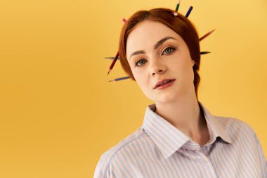 Göz alıcı bir kadın, sarı bir arka fona karşı saçında renkli kalemlerle güven içinde poz veriyor..