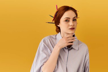 Genç bir kadın yaratıcı bir şekilde saçlarını kalemle şekillendiriyor, düşünceli bir şekilde poz veriyor..