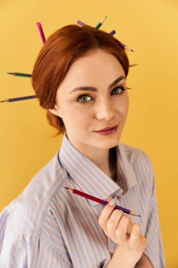 Neşeli, genç bir kadın saçlarını kalemle şekillendiriyor, yaratıcılığını sergiliyor..