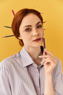 Canlı bir sahnede, çarpıcı bir kadın sanatsal yeteneklerini saçlarında renkli kalemlerle sergiliyor..