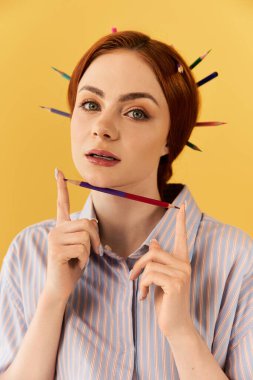 Kızıl saçlı genç bir kadın yüzünde renkli kalemlerle şakacı poz veriyor..