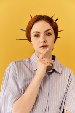 Sanatçı genç kadın saçlarına şık bir şekilde düzenlenmiş parlak kalemlerle düşünceli bir şekilde poz veriyor..