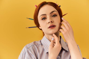 Genç bir kadın nazikçe yüzüne dokunuyor, saçları sarıya karşı renkli kalemlerle süslenmiş..