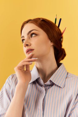 Kızıl saçlı ve kalemli genç bir kadın çizgili gömlek giyerken düşünceli bir şekilde dik dik bakıyor..