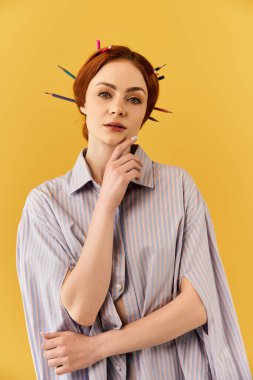 Genç bir kadın parlak sarı bir arkaplana karşı renkli kalemlerle düşünceli poz veriyor..