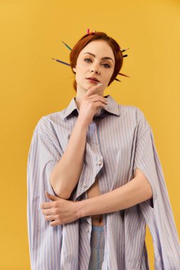 Güzel bir kadın nazikçe poz veriyor. Çenesi parmaklarının ucunda, sarı bir zemine dayanıyor..