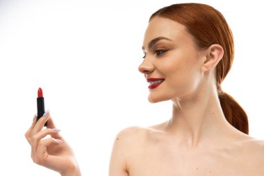 Çekici bir gülümsemesi olan genç bir kadın kırmızı ruj tutuyor, güzelliği ve kendini ifade etmeyi vurguluyor..