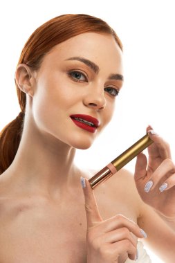 Çarpıcı özellikleri olan genç bir kadın yumuşak ışıkta şık bir dudak ürünü sergiliyor..