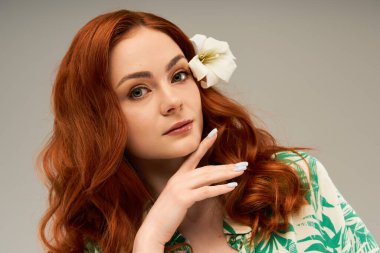 Çekiciliğini ve cazibesini sergileyen canlı kızıl saçlı büyüleyici genç bir kadın zarif bir poz verir..