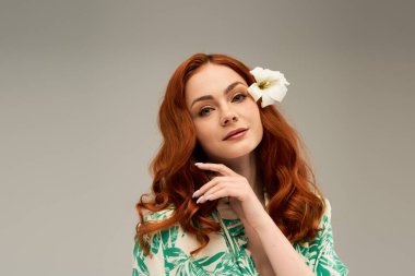 Kızıl saçlı ve kulağının arkasında çiçek olan genç bir kadın sıcak bir ortamda cazibe yayar..