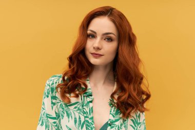 Göz kamaştırıcı genç bir kadın kırmızı saçlarını ve şık kıyafetini sergiliyor, kendine güveni ve cazibesi yayılıyor..