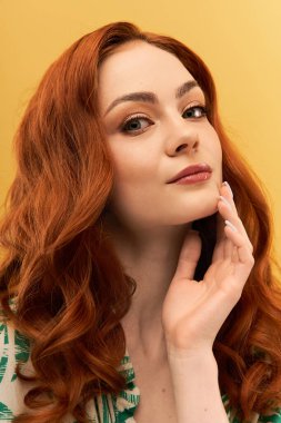 Dalgalı kırmızı bukleleri olan güzel bir kadın nazikçe yüzüne dokunur, kendinden emin bir şekilde..