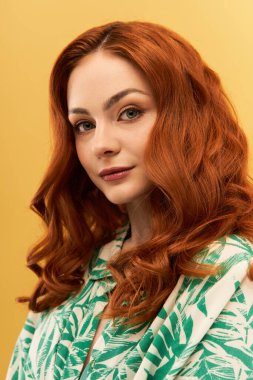 Kendine güveni tam genç bir kadın çarpıcı kızıl saçlarıyla sarı bir duvara doğru gülümsüyor..