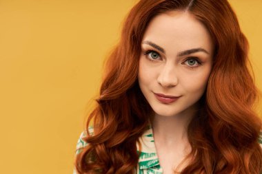 Güzel genç bir kadın büyüleyici kızıl saçlarını ve büyüleyici gözlerini nazikçe gülümserken sergiliyor..