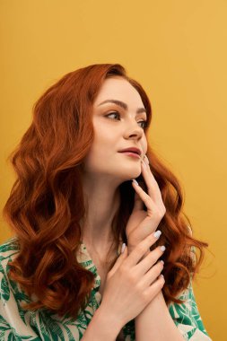 Dalgalı kızıl saçlı güzel bir kadın düşünceli bir şekilde yüzüne dokunuyor, kendine güveni tam..