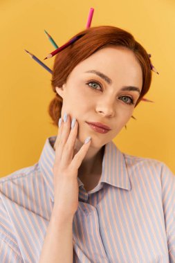 Çarpıcı özellikleri olan genç bir kadın sanatını canlı sarı bir arkaplanda sergiliyor..