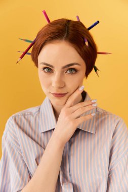 Genç bir kadın saçlarında kalemlerle özgüvenle poz veriyor. Yaratıcı bir yetenek ve tarz sergiliyor..