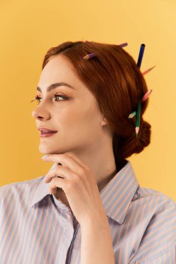 Güzel bir kadın düşünceli bir şekilde gülümserken saçlarını renkli kalemlerle şekillendirir..