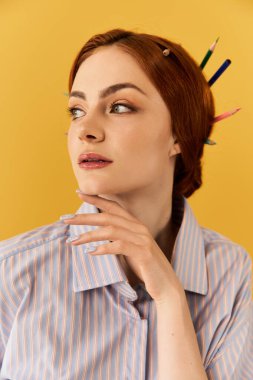 Genç ve hayat dolu bir kadın saçlarında kalemlerle yaratıcılığını sergiliyor, zarifçe gülümsüyor..