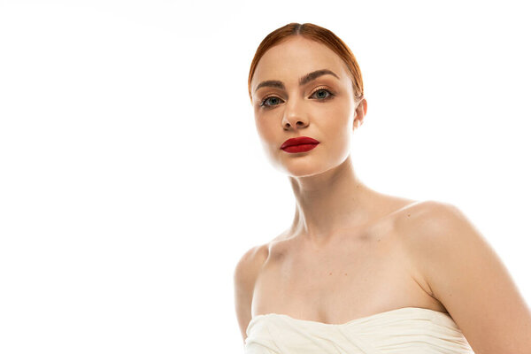 A beautiful young woman with striking features poses gracefully against a soft, bright backdrop.