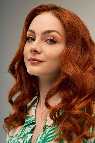 A young woman with flowing red hair and a warm smile exudes elegance.