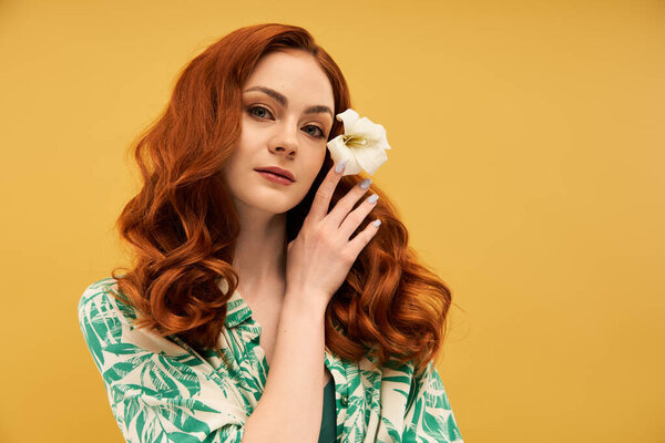 Молодая женщина касается волос, демонстрируя цветок на ярко-желтом фоне.