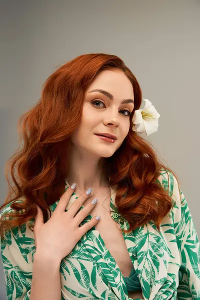 Güzel bir kadın, beyaz bir çiçekle süslenmiş dalgalı kızıl saçlarıyla özgüvenle poz verir..