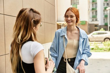 İki genç kadın dışarıda canlı sohbete girişiyor, şık kıyafetlerinin ve sıcak havanın tadını çıkarıyorlar..