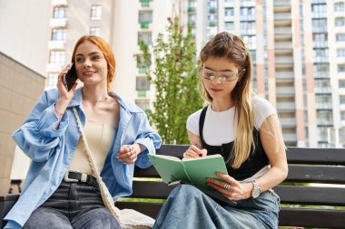 İki şık genç bayan açık hava bankında otururken keyifli bir sohbetten hoşlanırlar..